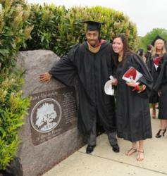 graduates posing by institution's seal on stone