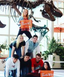 students posing with dinosaur skeleton and banners